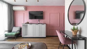 Un dormitorio moderno con paredes rosadas, un televisor de pantalla plana, un escritorio con espejo, una silla verde y una cama con una bandeja de vasos.