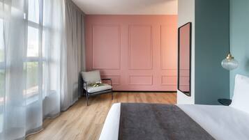 A bedroom with a bed, a chair, a window with sheer curtains, and a wall with a pink panel design.