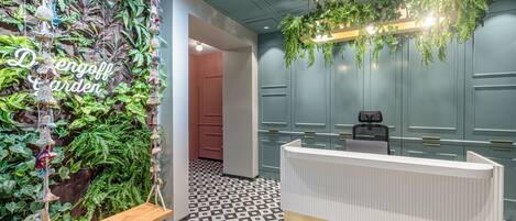 Un espace d’accueil au design moderne, avec un sol à motifs, un comptoir d’accueil et un mur orné de plantes suspendues et d’une enseigne indiquant « Jardin Dengoff ».