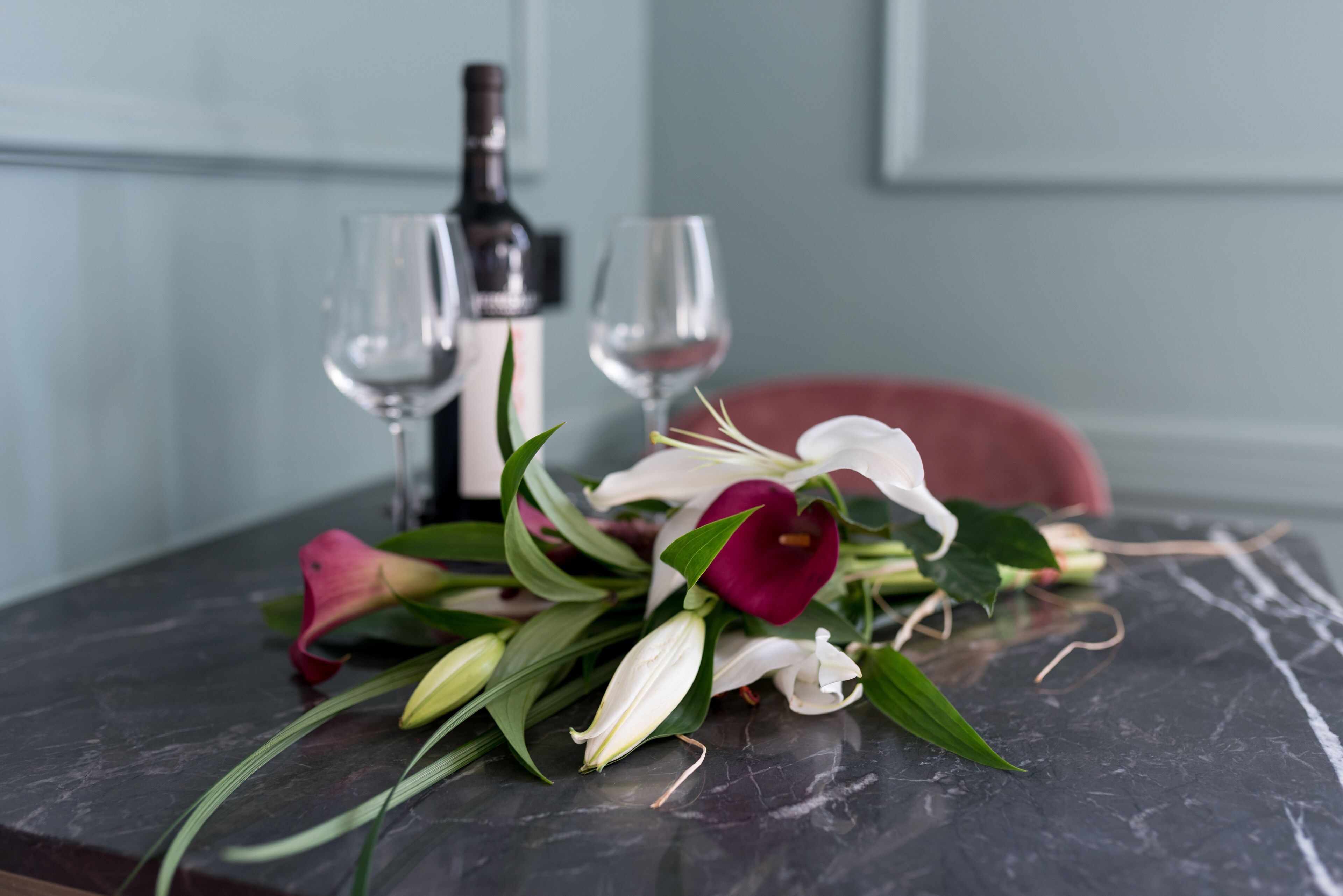 Una mesa con un ramillete de flores, dos copas de vino y una botella.