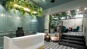Zona de recepción con un mostrador blanco, suelo con estampado blanco y negro y plantas colgantes verdes.