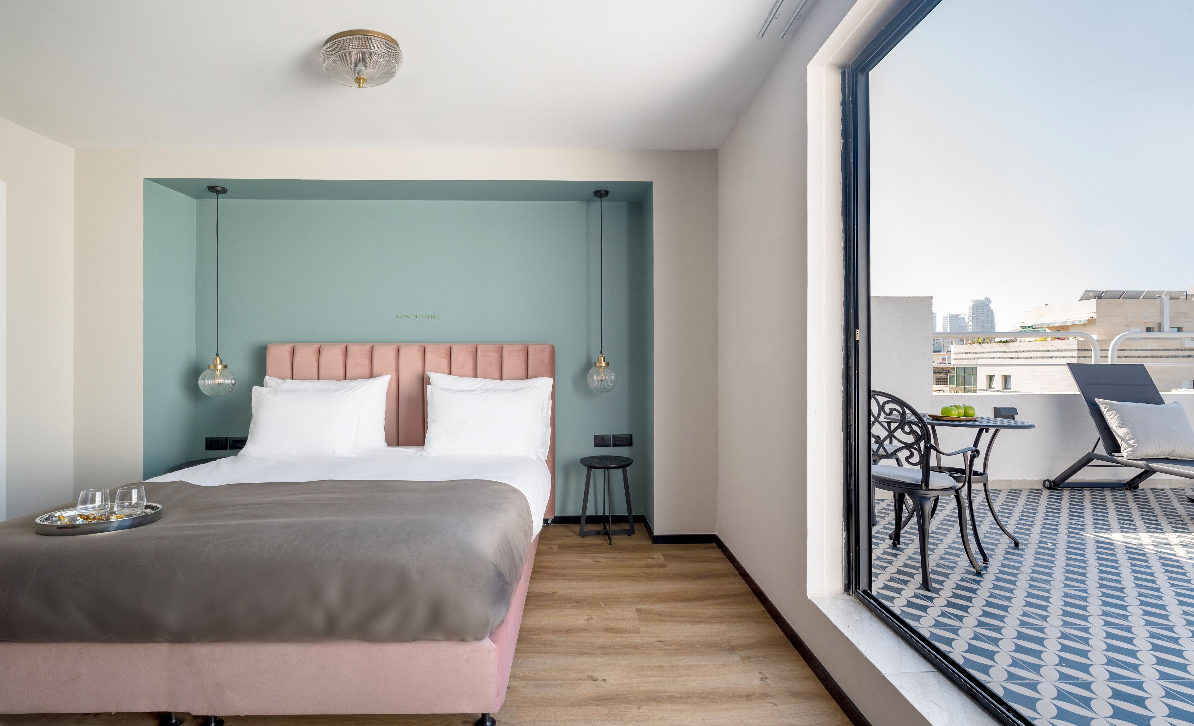 A hotel room with a bed, bedside tables, a small balcony with a table and chairs, and a city view.
