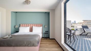 A hotel room with a bed, bedside tables, a small balcony with a table and chairs, and a city view.
