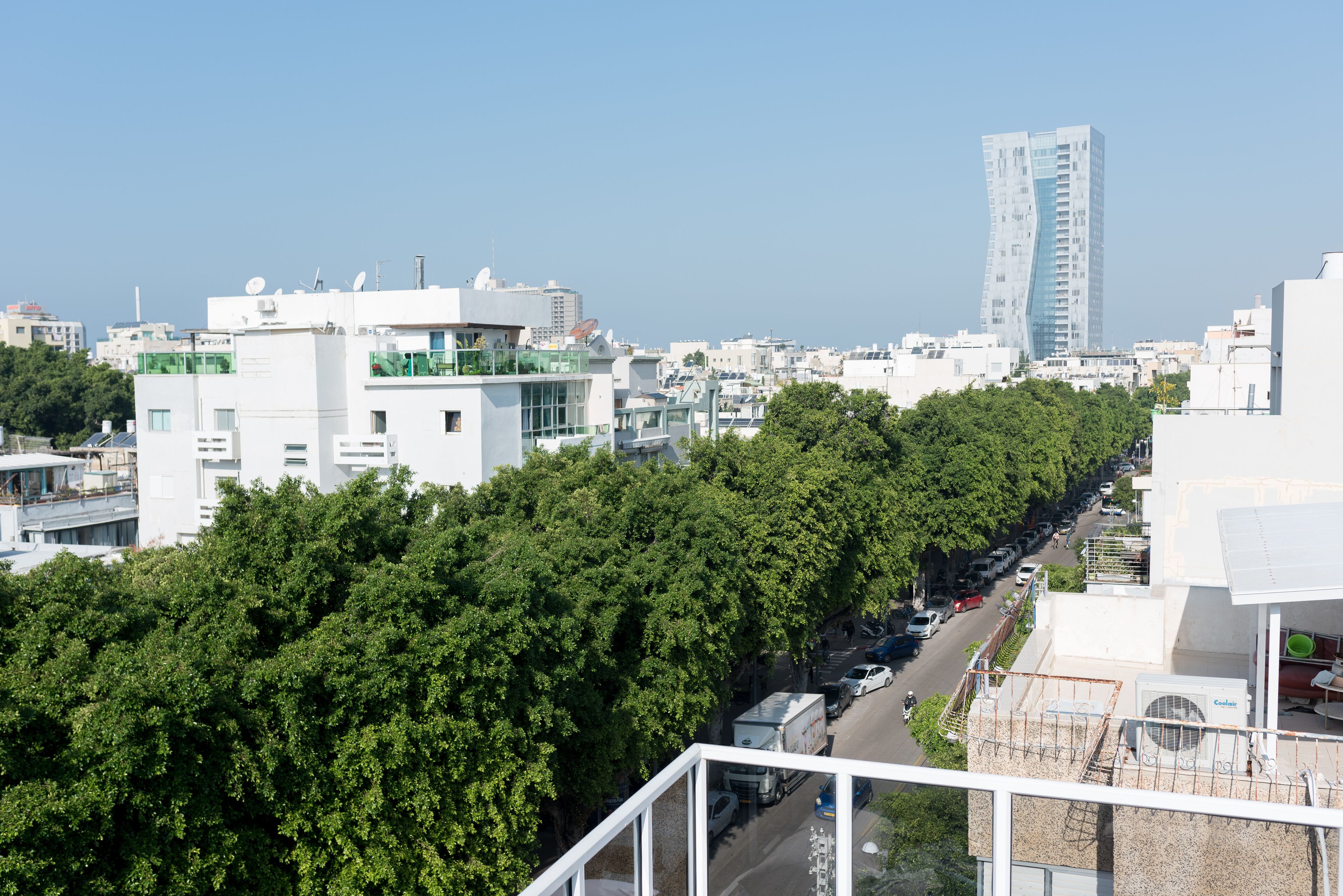 A cityscape with modern buildings, a prominent high-rise, and a tree-lined street.