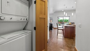 Una sala de lavandería con lavadora y secadora, una puerta de madera y vista hacia un comedor con mesa y sillas.