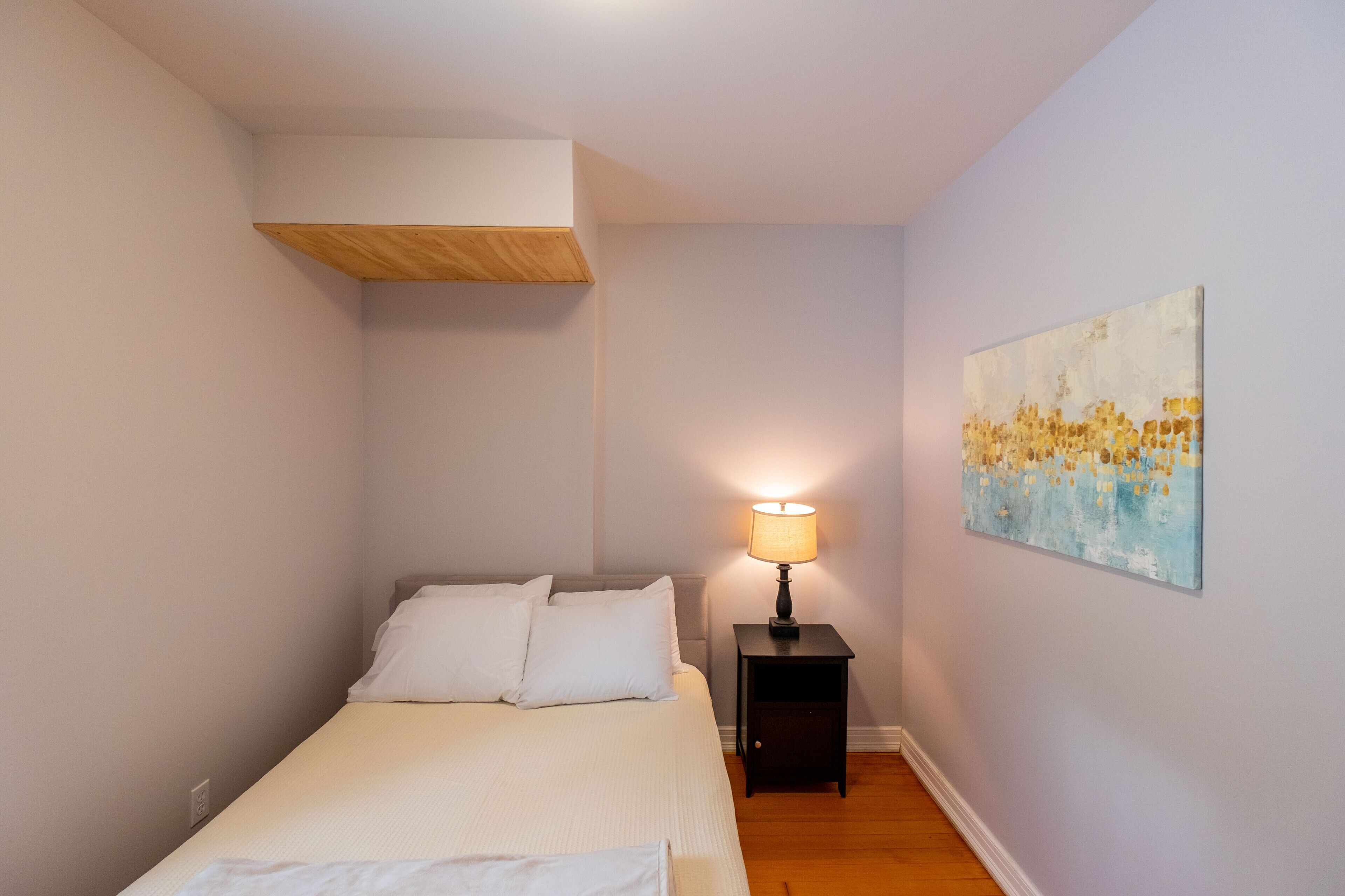 Une chambre à coucher avec un lit, une table de chevet avec une lampe et un tableau au mur.