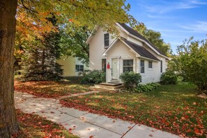 A single-story house with a front porch, a visible mailbox, and a well-maintained lawn with fallen leaves. - Beautiful Downtown Traverse City Home w/ Garage! (Traverse City)