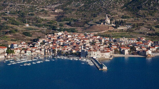 A coastal town with a dense cluster of buildings, a marina with numerous boats, and a prominent church on a hill. - Apartments Bepi-Apartment Roko (Komiža)