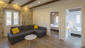 A modern living room with a grey sectional sofa, a round white table, and a stone wall. - Apartments Bepi-Apartment Roko (Komiža)