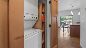 A laundry room with a washer and dryer, wooden shelving, and a view of a dining area with chairs and a table. - 57 Robber`s Roost #4 - Lionsback (Moab)