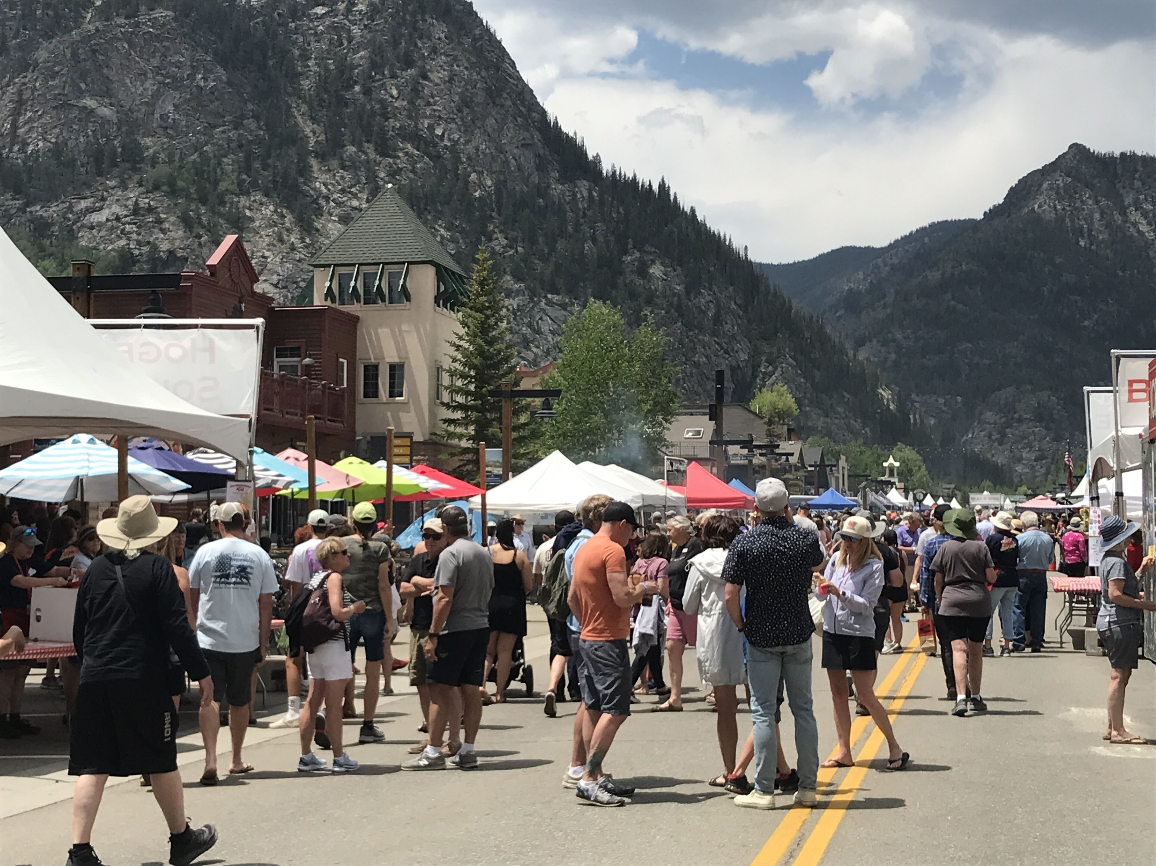 A crowded street with tents and people, set against a mountainous backdrop.