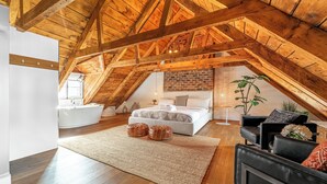 A bedroom with a sloped ceiling, a large bed, a white bathtub, and a wooden floor.