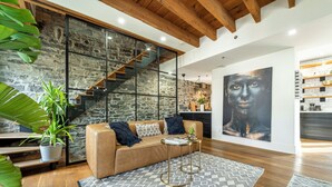 A modern living room with a stone wall, wooden staircase, and a large abstract painting.