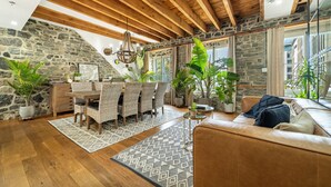 A spacious loft with exposed wooden beams, a stone wall, and a dining area with wicker furniture.