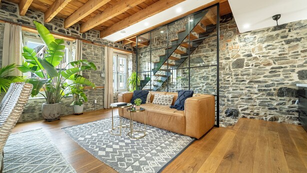 A cozy living room with a wooden ceiling, stone walls, a sofa, a coffee table, and a staircase.