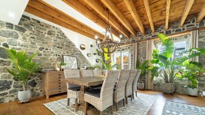 A dining area with a wooden table and wicker chairs, surrounded by potted plants and a stone wall.