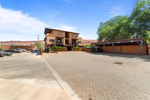 A hotel with a paved courtyard, multiple parking spaces, and a covered outdoor seating area.