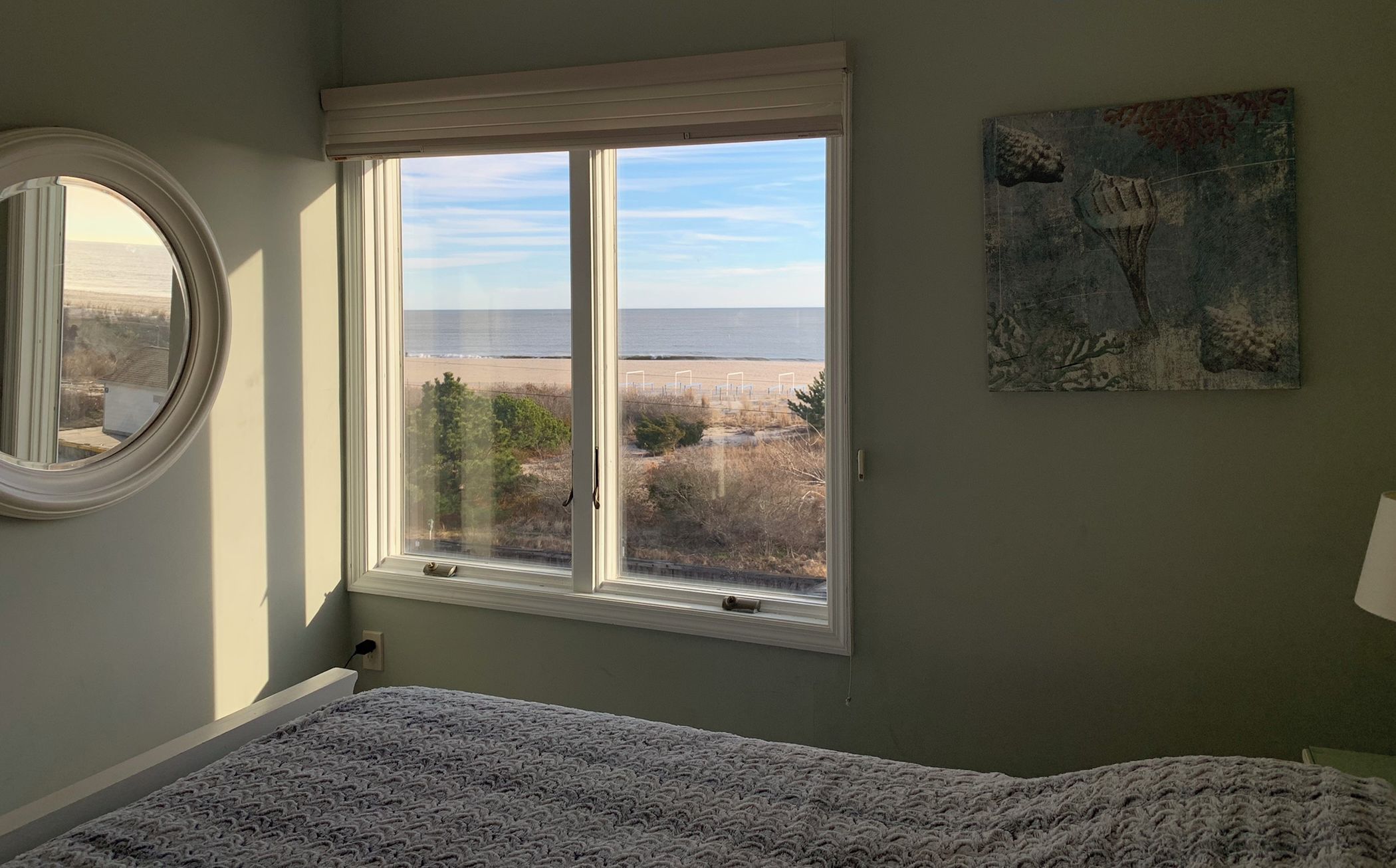 A bedroom with a large window offering a view of the beach and ocean.