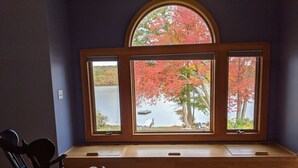 Een kamer met een groot raam met uitzicht op een meer en herfstkleurige bomen.