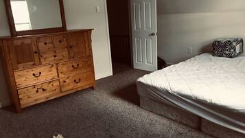 A bedroom with a wooden dresser, a bed with a patterned pillow, and a carpeted floor.