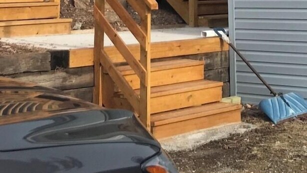Kaksikerroksinen puinen portaikko, joka johtaa parvekkeelle, jossa on kaide.