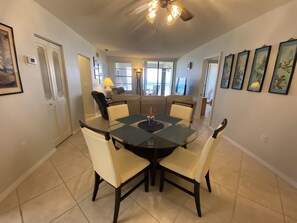 A dining area with a glass table surrounded by chairs, a ceiling fan, and a view of the living room through a glass door. - On the beach 4th Floor Direct Ocean Front Condo (Cocoa Beach)
