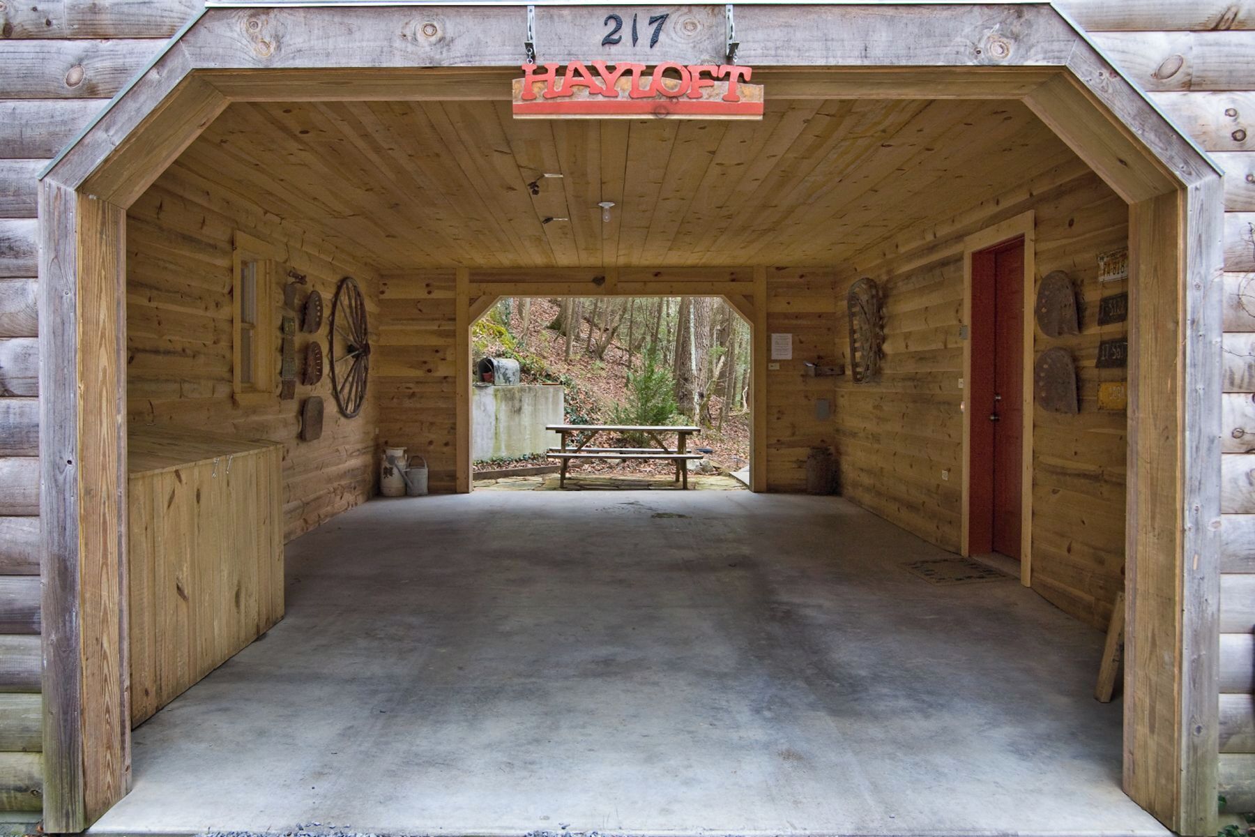 A wooden cabin with a covered entrance labeled "217 HAYLOFT". Inside, there is a picnic table and a door on the right.