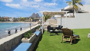 Eine Terrasse mit Blick auf Strand und Berge, ausgestattet mit einer Pergola, Sitzmöbeln im Freien und einem Pool.