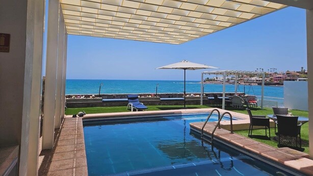 Ein Außenpool mit Meerblick, eine überdachte Lounge und eine Terrasse mit Tischen und Stühlen.