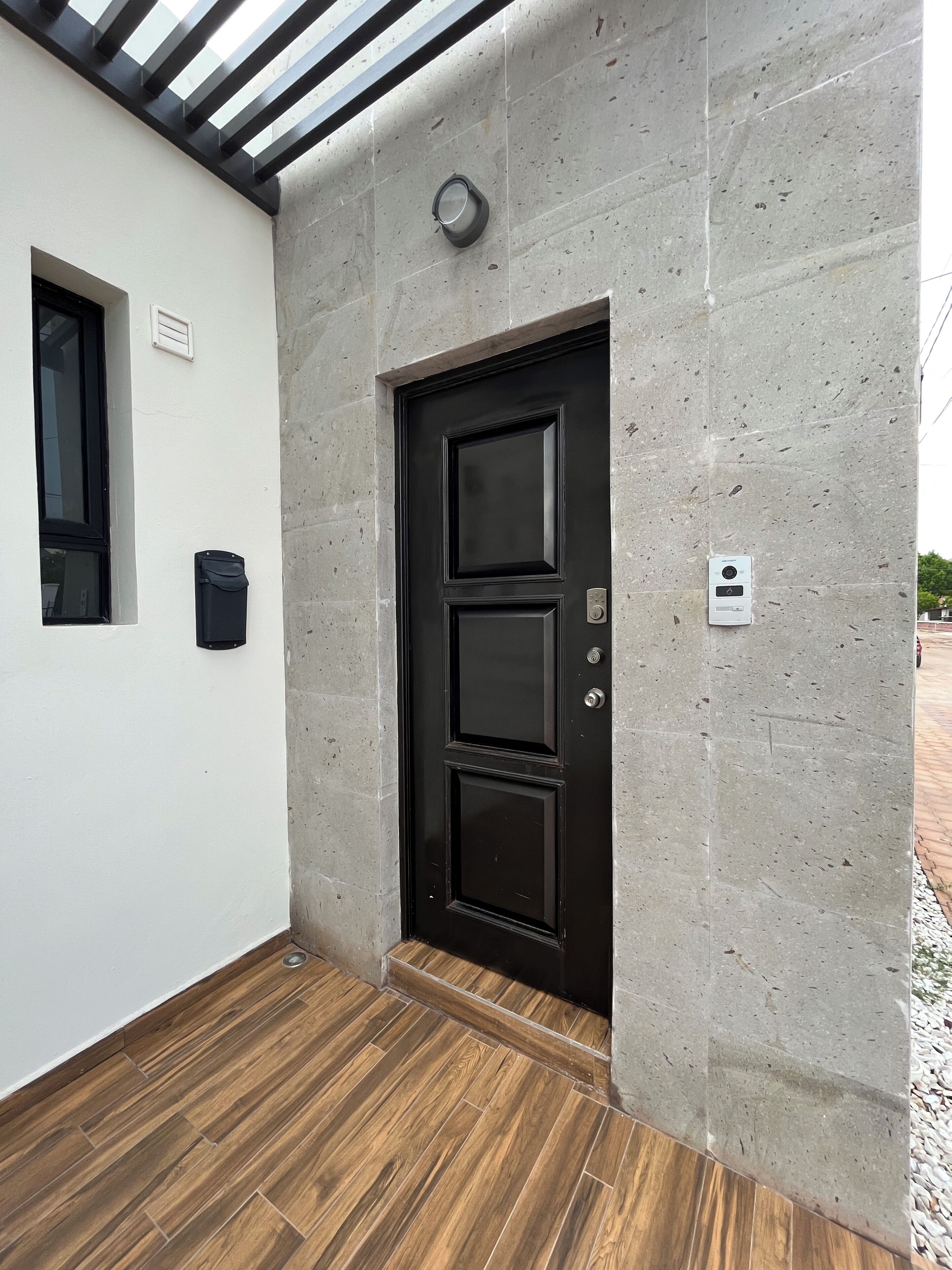 En sort dør med et kode lås, et lille vindue og en postkasse på en betonvæg.