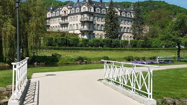 A pathway leading to a large, historic building with multiple balconies, surrounded by lush greenery and a well-maintained lawn. - Ferienwohnung Maria - Bad Kissingen (Bad Kissingen)