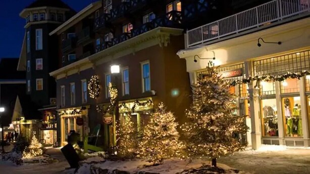 Un hôtel dont le sol est recouvert de neige, avec un sapin de Noël et une devanture ornée d’une enseigne.