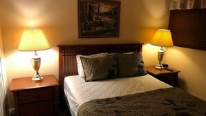 Un lit bien fait, avec une courtepointe et des oreillers, deux lampes de chevet, une table de nuit et un tableau accroché au mur.