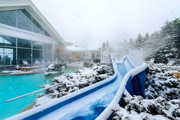 A snow-covered outdoor area with a pool, a blue slide, and a building with large windows.
