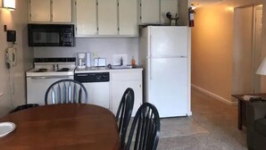 Une cuisine compacte avec des meubles blancs, un four à micro-ondes, une cuisinière et un réfrigérateur. On y trouve également une table à manger avec des chaises.