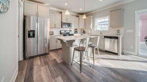 Una cocina moderna con electrodomésticos de acero inoxidable, una isla central con taburetes de bar e iluminación colgante.