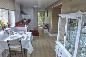 Un comedor con una mesa preparada para cuatro personas, una cocina al fondo y un armario de vidrio con vajilla.