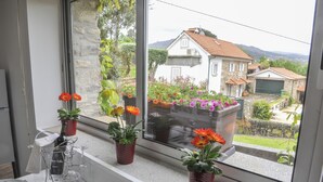 Una zona de menjador amb una taula preparada per a dues persones, una finestra amb plantes en testos i una vista d'una casa i un jardí.