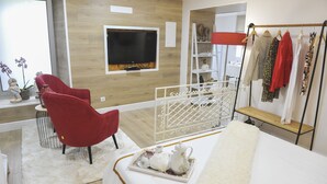 Habitació moderna amb televisió, cadira vermella, taula blanca i joc de te, i una estant per a roba.