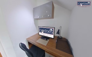 A small office space with a desk, a chair, a computer, a lamp, and a sign advertising Covstays serviced apartments in Coventry Central.