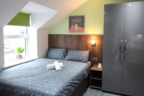 Een slaapkamer met een bed, nachtkastje, kledingkast, raam met uitzicht en een wandlamp.