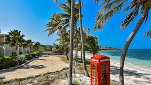 En strand med palmer, en rød telefonkiosk og en klar blå himmel.