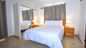 Et hotelværelse med en stor seng, to sengeborde med lamper, et spejl og en dør til et andet rum.