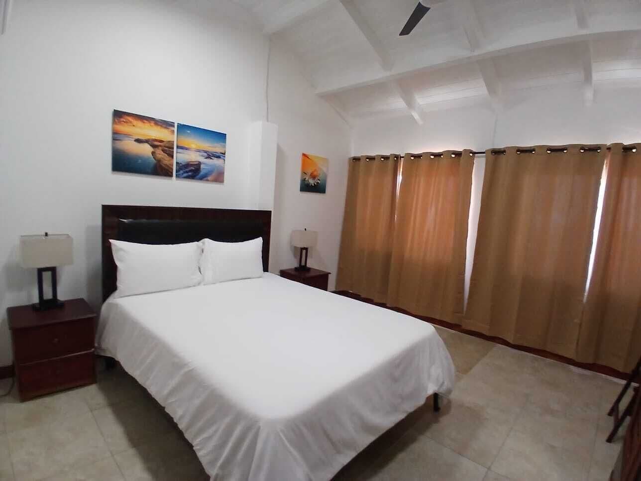 Quarto de hotel com uma cama, duas mesas de cabeceira e uma janela com cortinas.