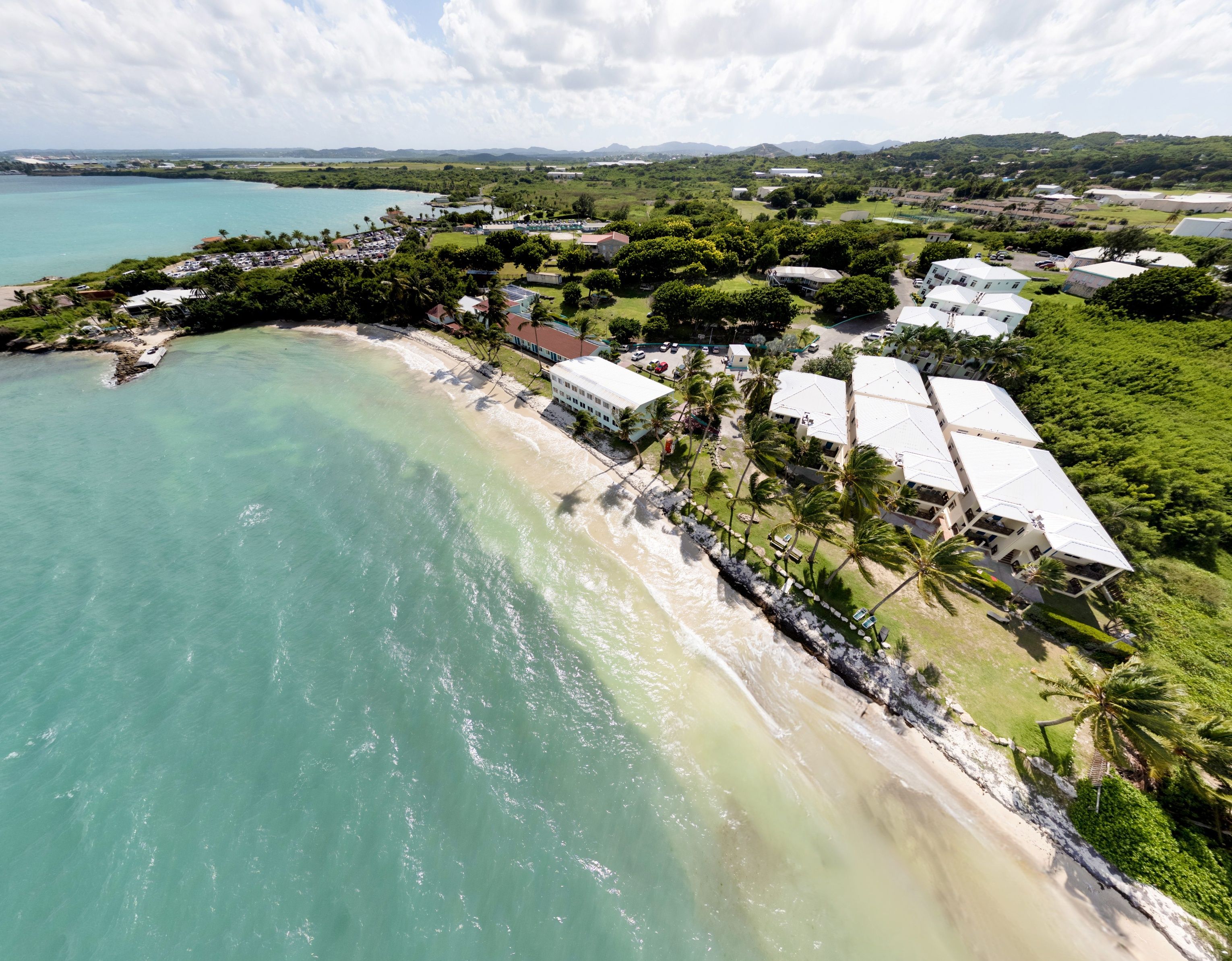 An aerial view of a coastal area with a beach, buildings, and greenery.