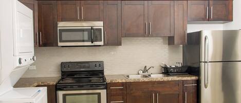 A kitchen with dark wooden cabinets, a stainless steel refrigerator, a microwave, an oven, and a sink.