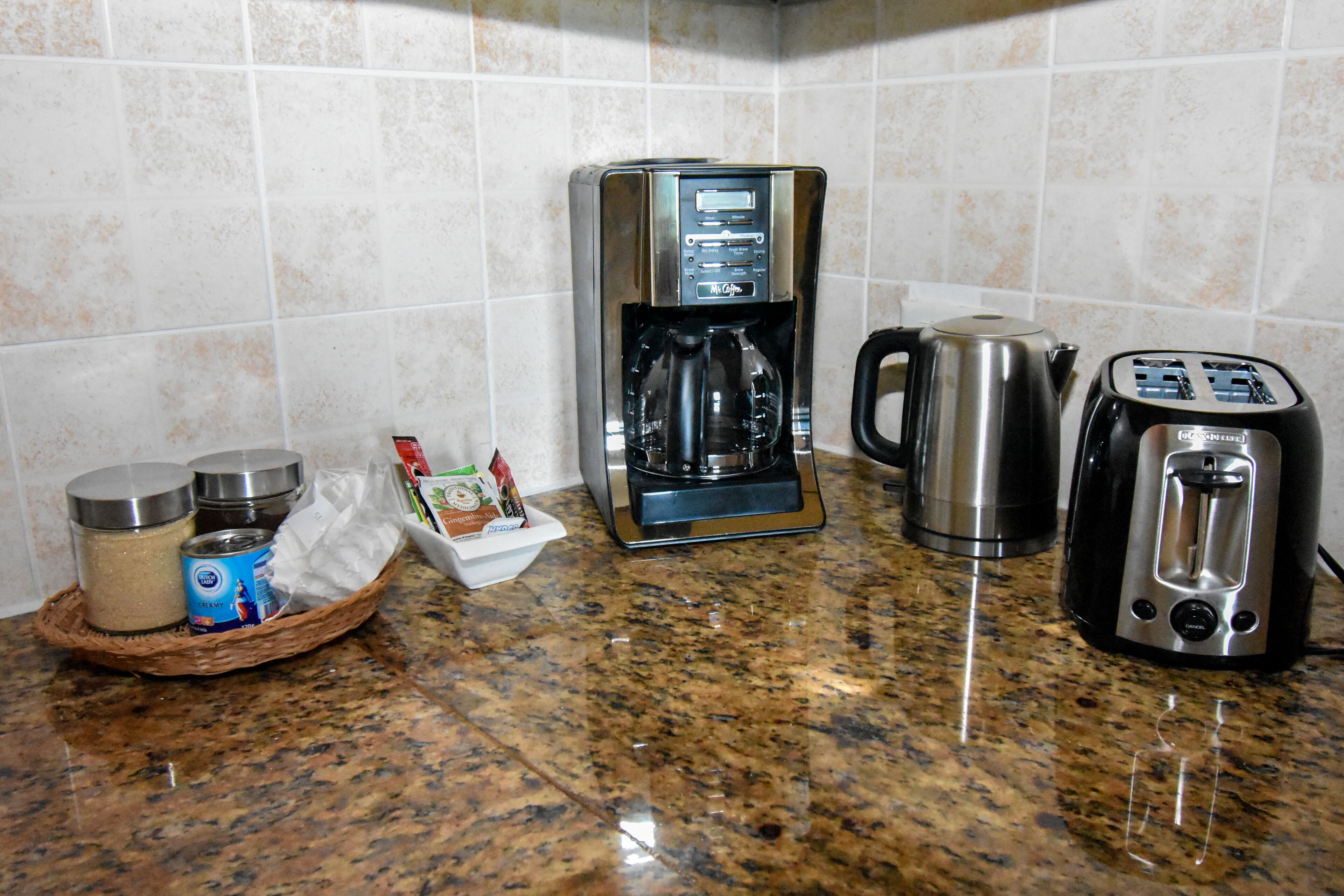 A kitchen with a coffee maker, toaster, kettle, and a basket containing condiments and a can.
