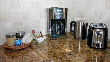 Una cocina con cafetera, tostadora, hervidor y una cesta que contiene condimentos y una lata.