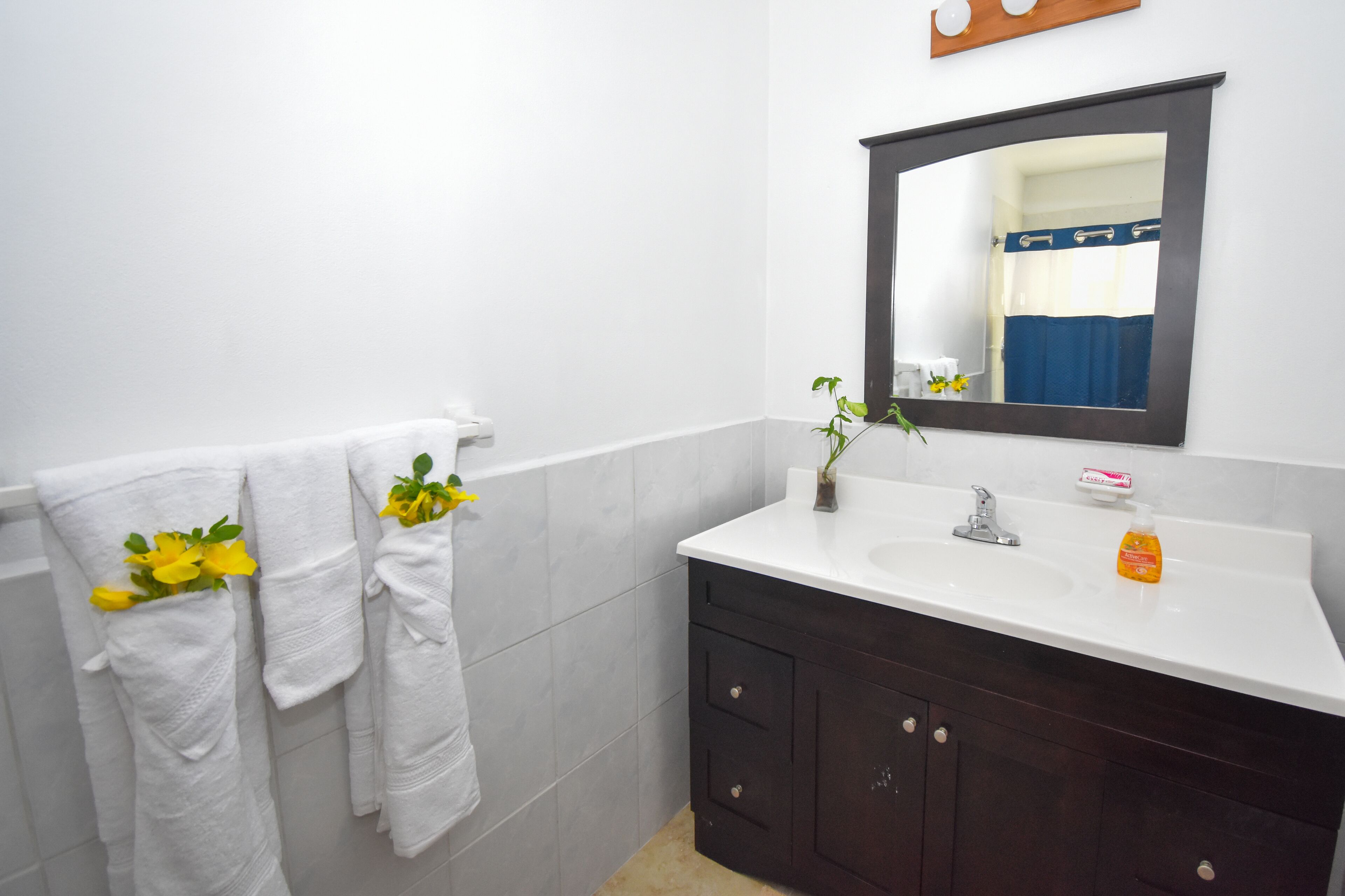 Un baño con azulejos blancos, un mueble de tocador de madera oscura, un lavabo blanco y un espejo encima.