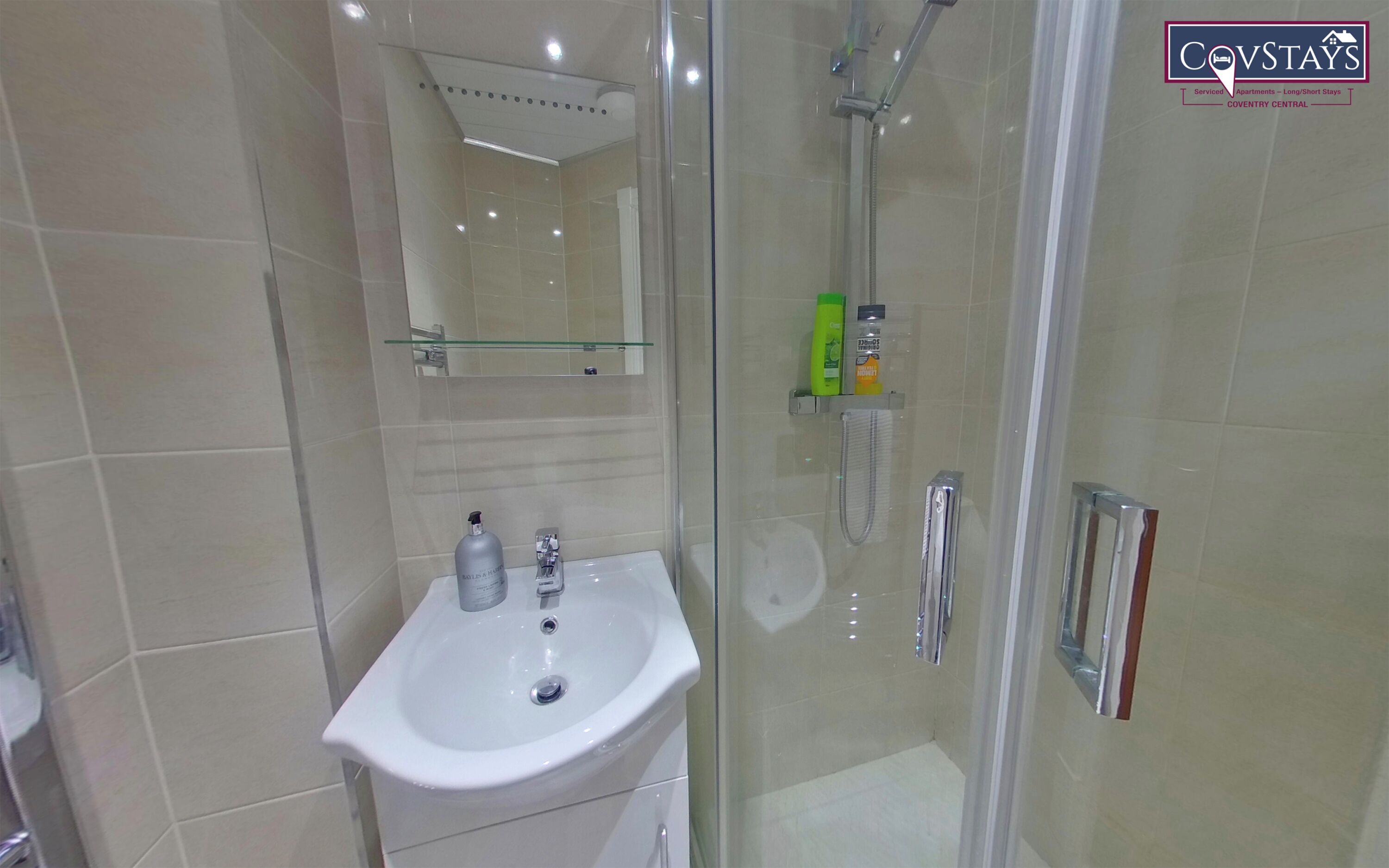 A modern bathroom with a glass shower enclosure, a white sink, and toiletries.